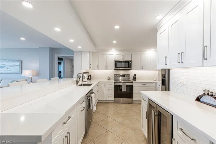 Kitchen featuring stainless steel appliances, a sink, tasteful backsplash, light stone counters, and beverage cooler