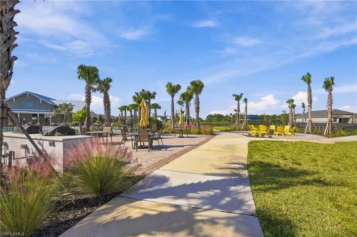 Paver patio featuring a built-in outdoor kitchen, concrete walkways, manicured lawn, and mature palm trees