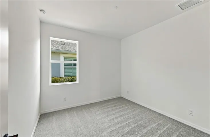 Neutral-toned interior space featuring light-colored wall paint, textured wall-to-wall carpeting, and a single-pane window