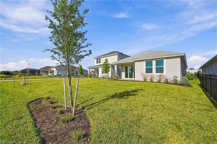 Stucco exterior residence featuring a covered patio, expansive lawn, mulch landscaping beds, and a perimeter privacy fence