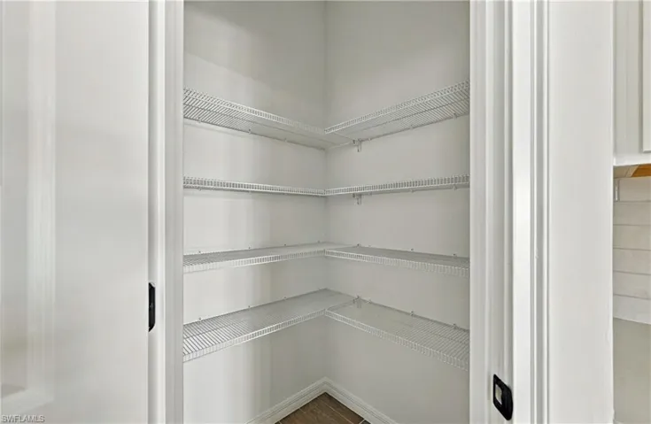 Walk-in storage space featuring multi-level white wire shelving and wood-finish flooring