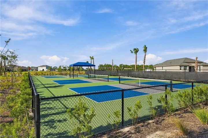 Multi-court athletic facility featuring blue and green hard surfaces, perimeter chain-link fencing, and a covered pavilion