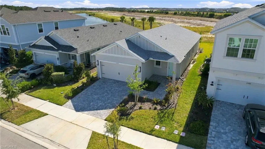 Single-story residence featuring light-toned siding, a multi-gabled roofline, paver driveway, and professional landscaping