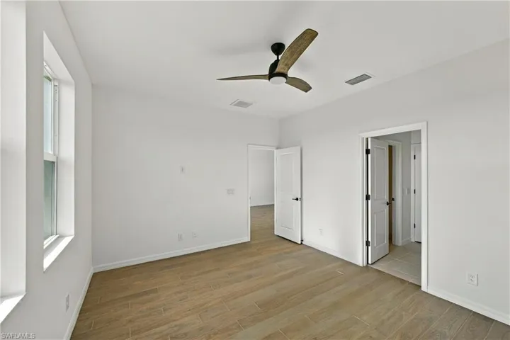 Interior space featuring wood-finish tile flooring, white walls, and a modern ceiling fan with three wood-toned blades
