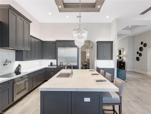 Kitchen featuring light stone counters, a breakfast bar area, gray cabinets, a center island with sink, and a high ceiling