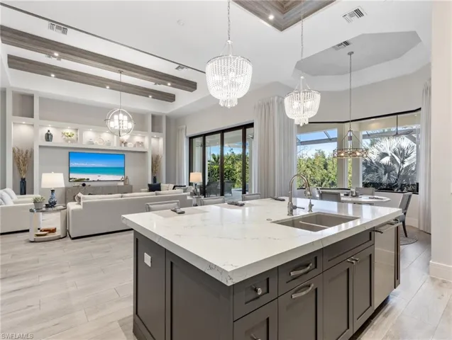 Kitchen featuring hanging light fixtures, a raised ceiling, light stone counters, a center island with sink, and a high ceiling