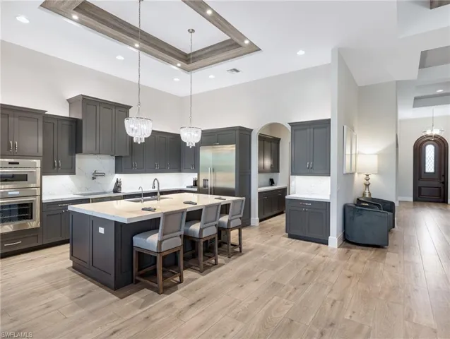Kitchen featuring a kitchen bar, decorative backsplash, pendant lighting, a tray ceiling, and a high ceiling