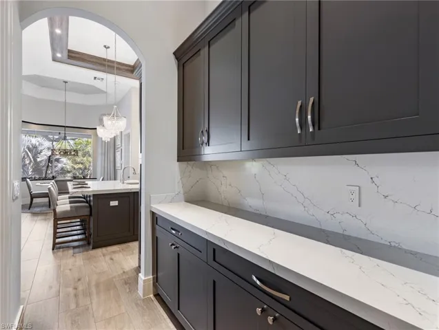 Bar area with light stone counters, a raised ceiling, crown molding, pendant lighting, and tasteful backsplash