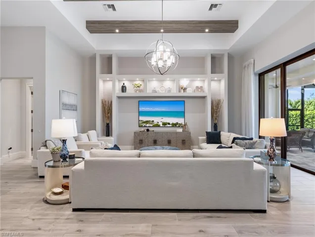 Living room featuring a raised ceiling, light wood-style floors, a high ceiling, a chandelier, and recessed lighting