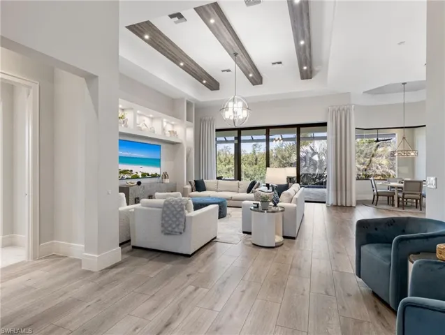Living room with a chandelier, light wood-style floors, a raised ceiling, and a high ceiling