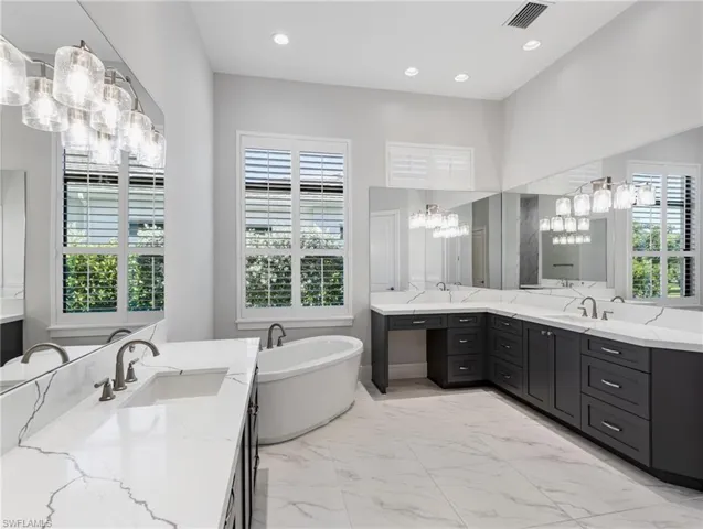 Bathroom featuring two vanities, a freestanding tub, light marble finish flooring, recessed lighting, and a chandelier
