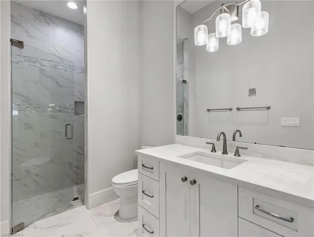 Bathroom featuring vanity, a marble finish shower, and light marble finish flooring