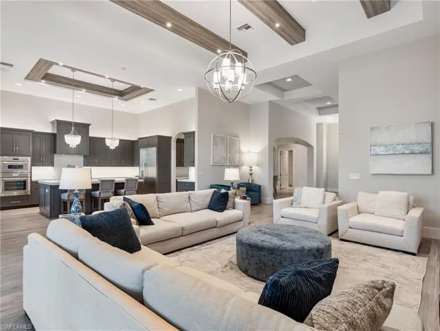 Living area with light wood-style floors, a chandelier, arched walkways, a raised ceiling, and a towering ceiling