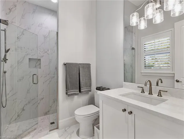 Bathroom featuring vanity, a marble finish shower, and marble look tile flooring