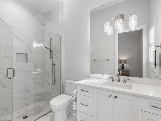 Bathroom featuring vanity, a marble finish shower, ensuite bathroom, and light marble finish flooring