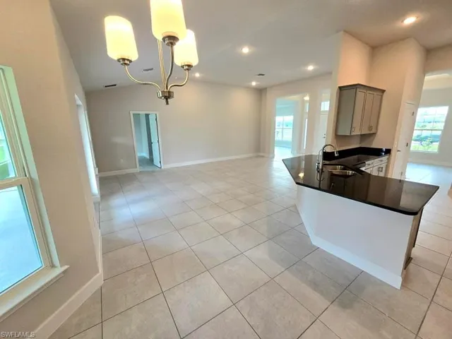 Kitchen with hanging light fixtures, kitchen peninsula, sink, light tile patterned flooring, and gray cabinets