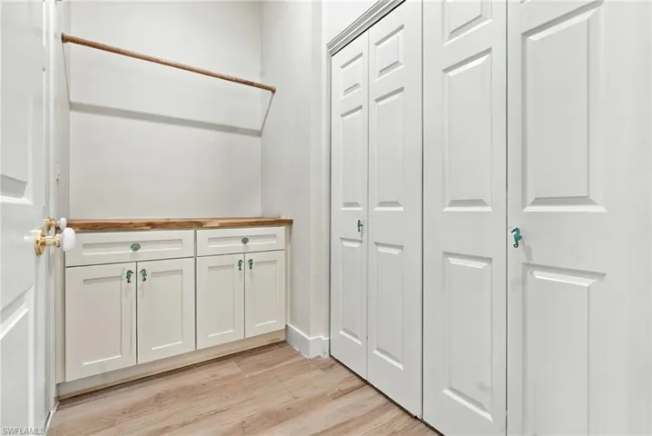 Built-in cabinetry featuring white shaker-style doors, wood-finish countertop, wood-finish flooring, and floor-to-ceiling bi-fold closet doors
