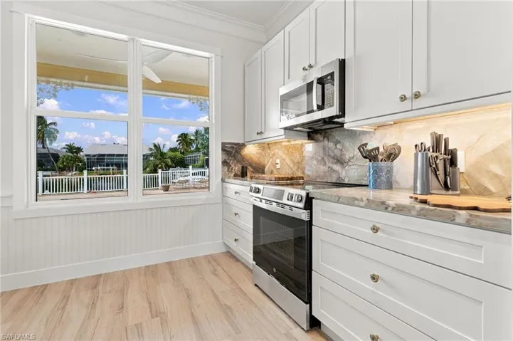 Kitchen featuring white cabinetry, wood-finish flooring, stone-surfaced countertops, a full-height stone backsplash, and stainless steel appliances