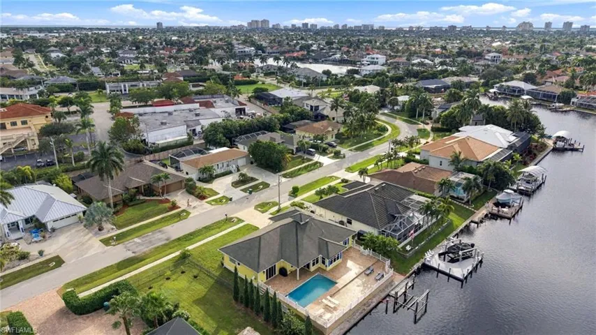Aerial perspective of waterfront property featuring a private swimming pool, concrete boat dock, paved deck, and tile roofing