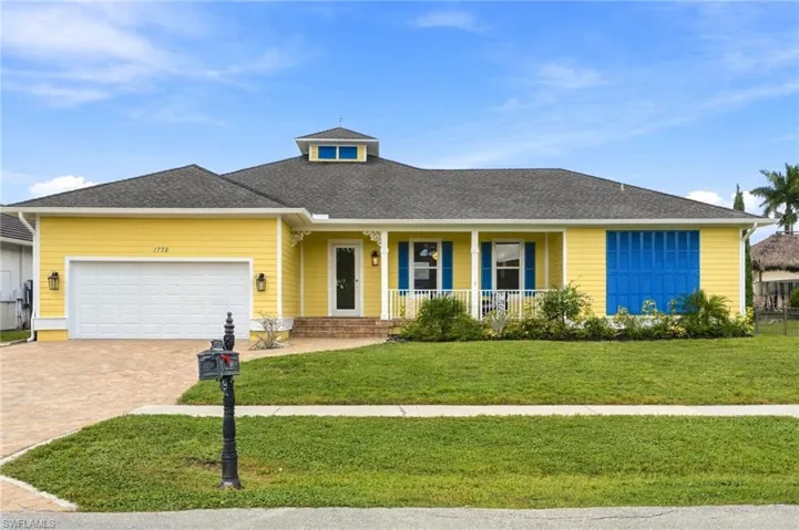 Single-story exterior featuring a hip roof with a central cupola, horizontal siding, a covered front porch with decorative brackets, a multi-car garage, and a paver driveway