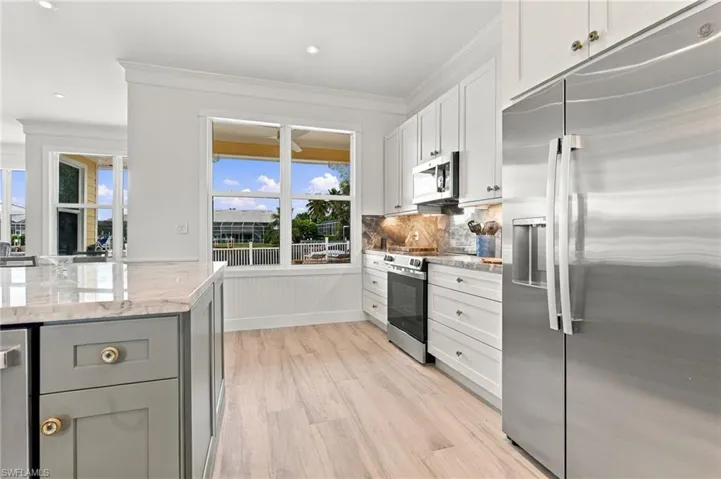 Kitchen featuring white shaker-style cabinetry, stainless steel appliances, a center island with light-toned stone countertops, and wood-finish flooring
