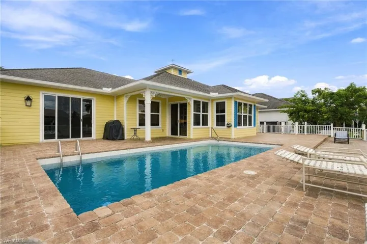 Exterior rear elevation featuring lap siding, a covered patio area, a concrete paver pool deck, and an in-ground swimming pool with metal ladder access