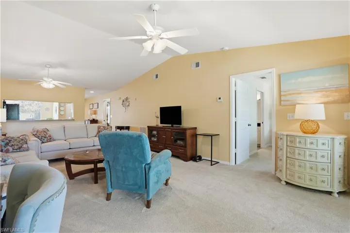 Living area featuring light colored carpet, lofted ceiling, and a ceiling fan
