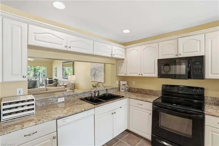 Kitchen with black appliances, white cabinets, decorative light fixtures, a center island, and a chandelier