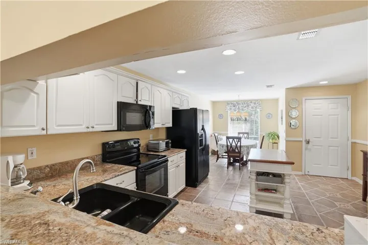 Kitchen with black appliances, white cabinets, recessed lighting, light stone counters, and light tile patterned flooring