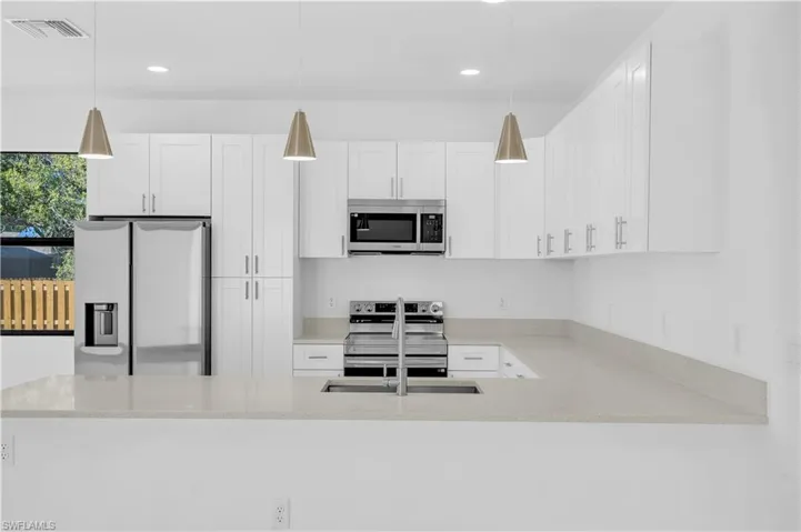 Kitchen with stainless steel appliances, white cabinetry, pendant lighting, light stone countertops, and a peninsula