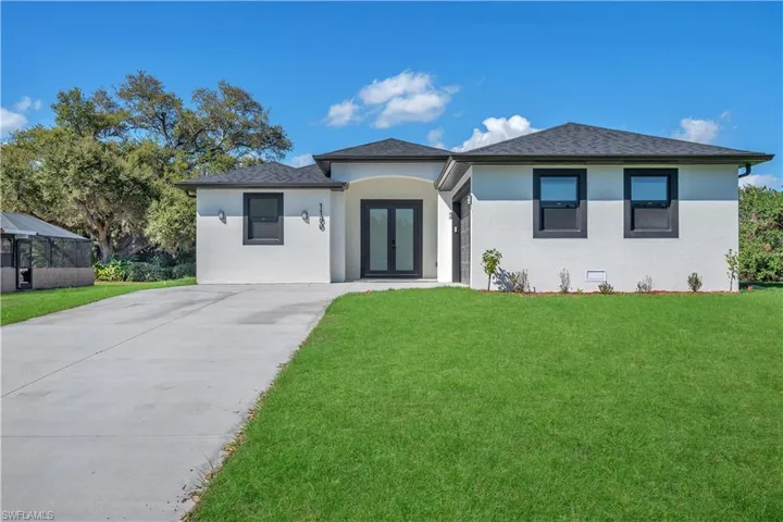 View of front of home with a front yard, stucco siding, french doors, and concrete driveway