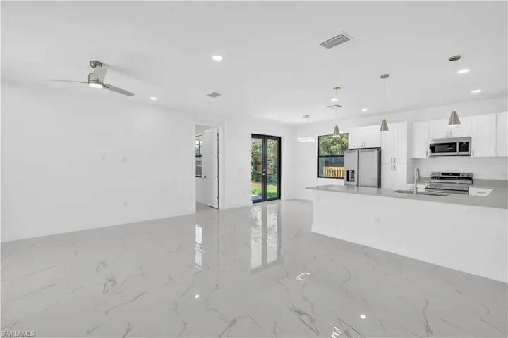 Kitchen featuring white cabinets, stainless steel appliances, light stone countertops, a ceiling fan, and open floor plan