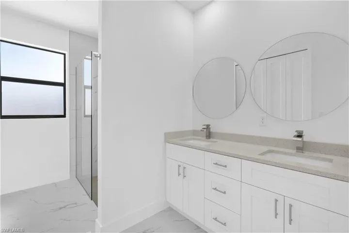 Bathroom featuring double vanity, light marble finish floors, and a marble finish shower