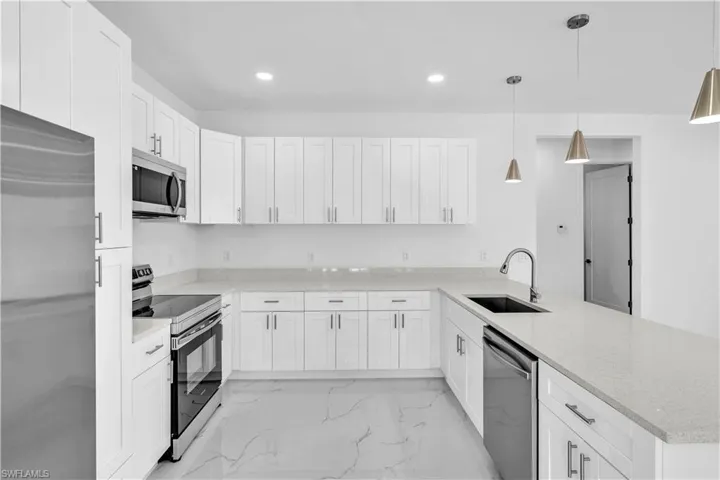 Kitchen featuring stainless steel appliances, white cabinetry, light stone counters, and a peninsula