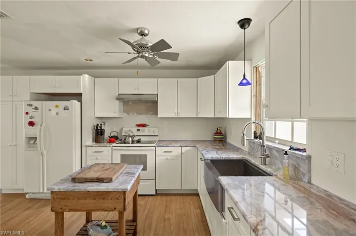 Kitchen with white appliances, light stone countertops, decorative light fixtures, light wood-type flooring, and white cabinetry