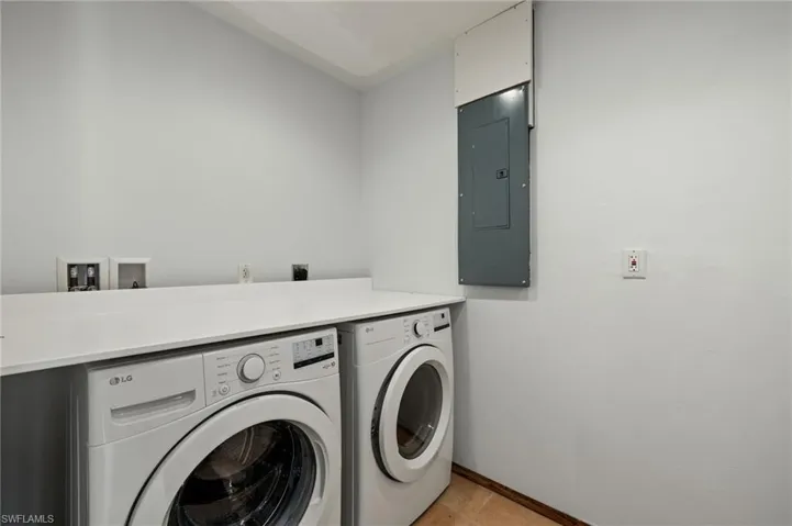 Clothes washing area with electric panel, washer and clothes dryer, and light tile patterned floors