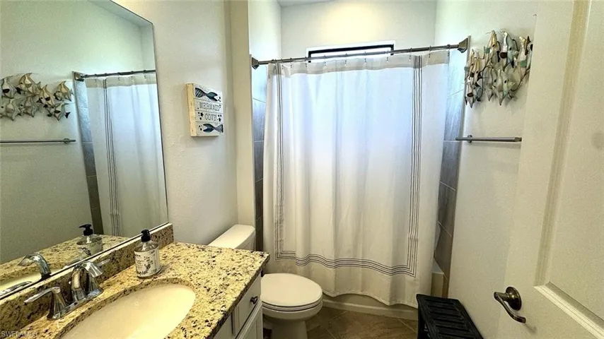 Full bath featuring vanity, shower / tub combo with curtain, and dark tile patterned floors