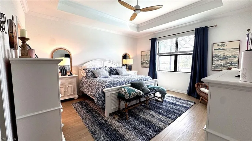 Bedroom featuring light wood-style flooring, a raised ceiling, a ceiling fan, and ornamental molding
