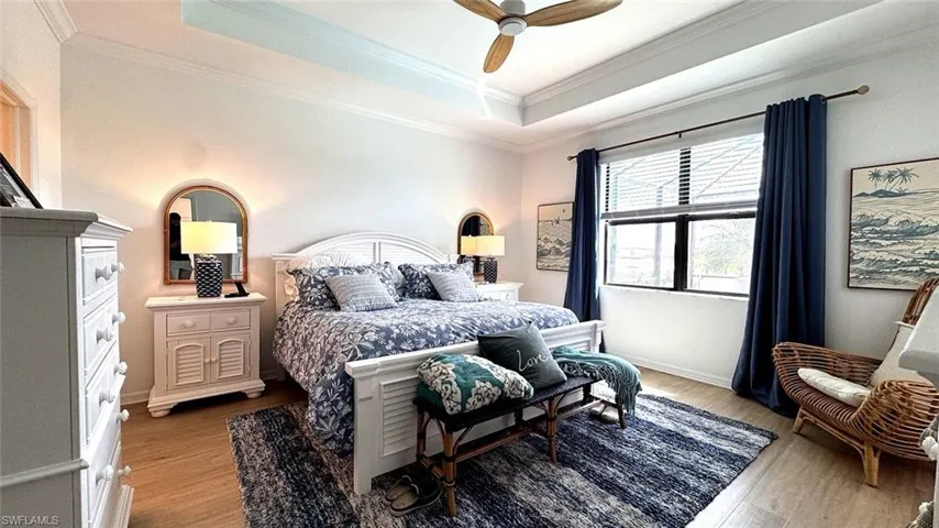 Bedroom featuring light wood-style flooring, ceiling fan, a tray ceiling, and ornamental molding