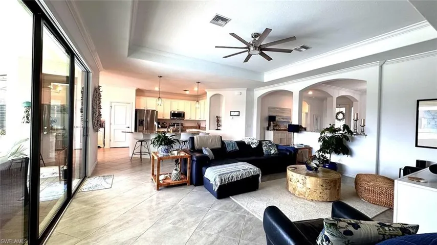 Living room featuring arched walkways, ceiling fan, a raised ceiling, light tile patterned floors, and crown molding