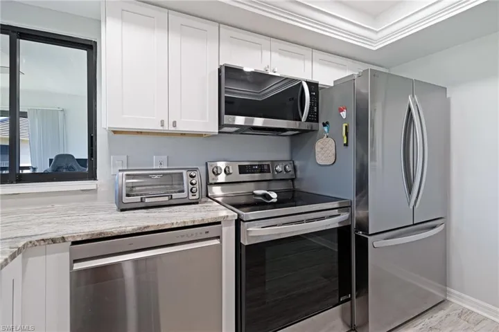 Kitchen with white cabinetry, light wood-type flooring, stainless steel appliances, baseboards, and a toaster