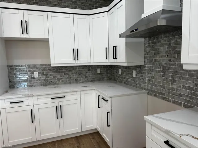 Kitchen with dark wood-type flooring, white cabinetry, wall chimney range hood, decorative backsplash, and light stone countertops