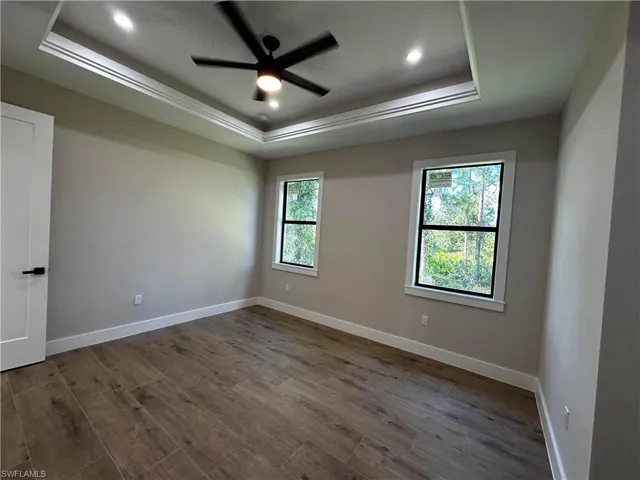 Empty room with wood-type flooring, a tray ceiling, and ceiling fan
