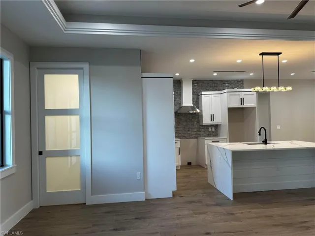 Kitchen featuring hanging light fixtures, sink, wood-type flooring, wall chimney range hood, and white cabinetry