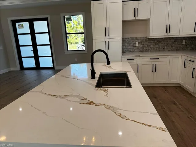 Kitchen featuring light stone counters, sink, dark wood-type flooring, and tasteful backsplash