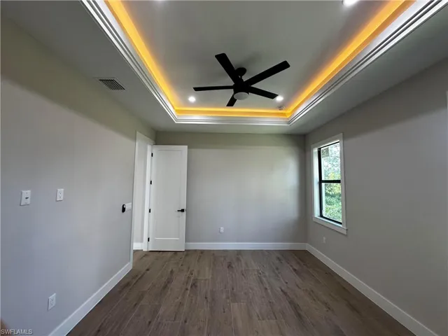 Unfurnished room featuring ceiling fan, a raised ceiling, and dark wood-type flooring