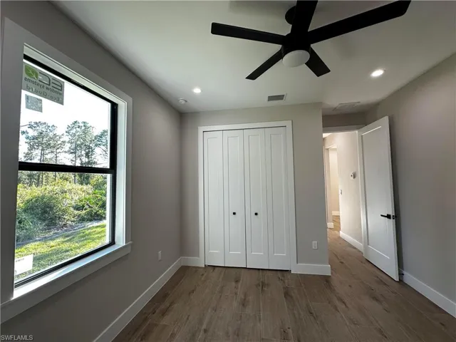 Unfurnished bedroom featuring ceiling fan, a closet, dark hardwood / wood-style floors, and multiple windows