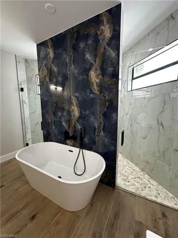 Bathroom with independent shower and bath, tile walls, and hardwood / wood-style flooring