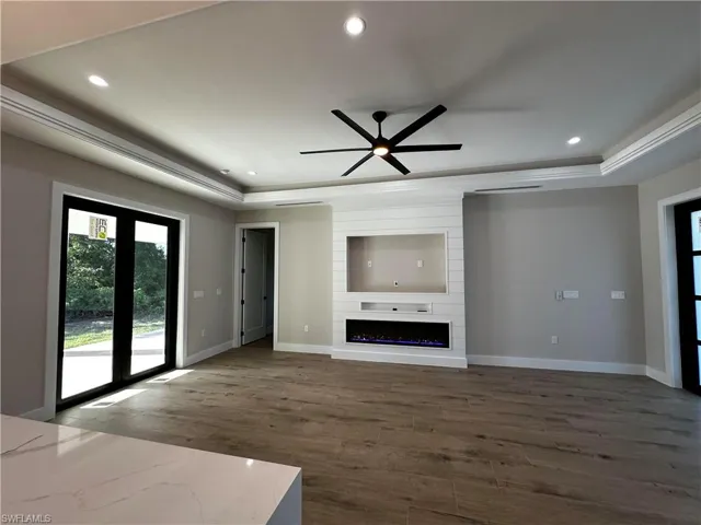 Unfurnished living room featuring ceiling fan, hardwood / wood-style flooring, ornamental molding, and a large fireplace