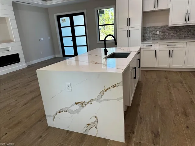 Kitchen featuring tasteful backsplash, sink, white cabinets, a center island with sink, and light stone countertops
